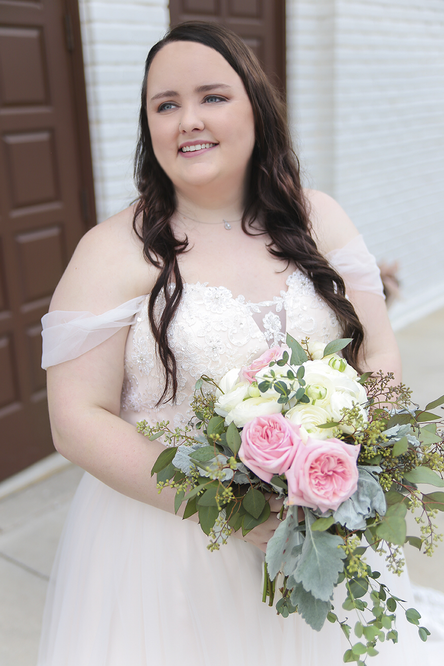 A bride in a blush dress holding her bouquet in a bridal portrait in front of Darlington Chapel in El Reno, Oklahoma